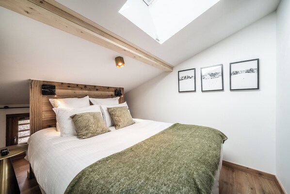 A bedroom with a skylight, a wooden headboard, a bed with white linens, and three framed pictures on the wall. - Colibri - Cozy Apartment in Les Gets (Les Gets)