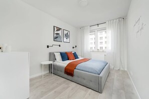 A bedroom with a bed, a small white table, and a window with curtains.