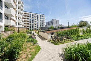 A modern apartment complex with a paved courtyard, bicycles, and a small garden area.