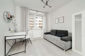 A modern living room with a white desk, a grey sofa, a white radiator, and a window with curtains.