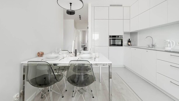 A modern kitchen with white cabinetry, a central island with chairs, and a dining table set for four.