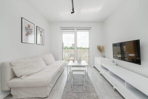 A modern living room with a white sofa, a coffee table, a flat-screen TV, and artwork on the wall.