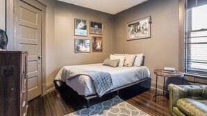 A bedroom with a bed, a dresser, a window with blinds, and wall art.