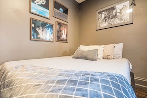 A bedroom with a bed, pillows, and four framed pictures on the wall.
