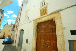 A narrow street with a large wooden door, a blue car parked on the side, and a building with a white facade. - Villa in Ostuni's White City (Ostuni)