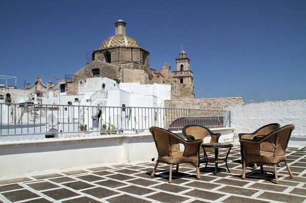A rooftop terrace with wicker furniture and a view of historic buildings.