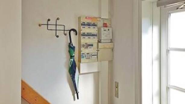 Un couloir avec un porte-manteau, une boîte électrique fixée au mur et une porte.