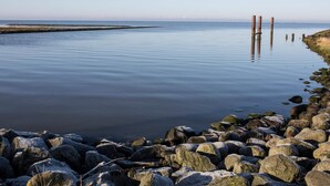 Un plan d'eau calme, avec une rive rocheuse et des poteaux en bois visibles au loin.