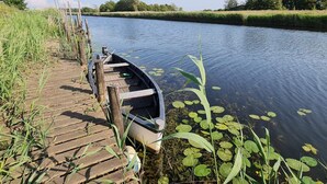 Une jetée en bois s’avance dans un fleuve paisible, et une petite barque est amarrée à son extrémité.
