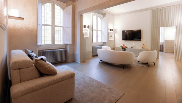 Een ruime woonkamer met een beige bank, een witte fauteuil en een groot raam.