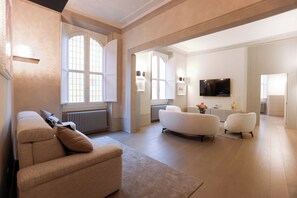 A spacious living room with a beige sofa, a white armchair, and a large window.