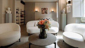 Een moderne woonkamer met een ronde salontafel, witte banken, een vaas met bloemen en een boekenkast.