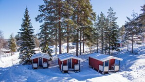 Three cabins with red exteriors and white trim, surrounded by snow-covered ground and tall evergreen trees. - Gopshusgården - Rum och Stugor (Mora)