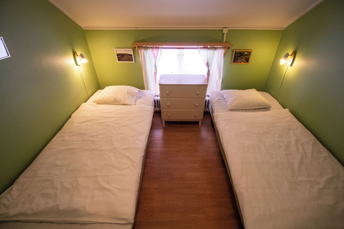 A room with two beds, a dresser, and a window with curtains.