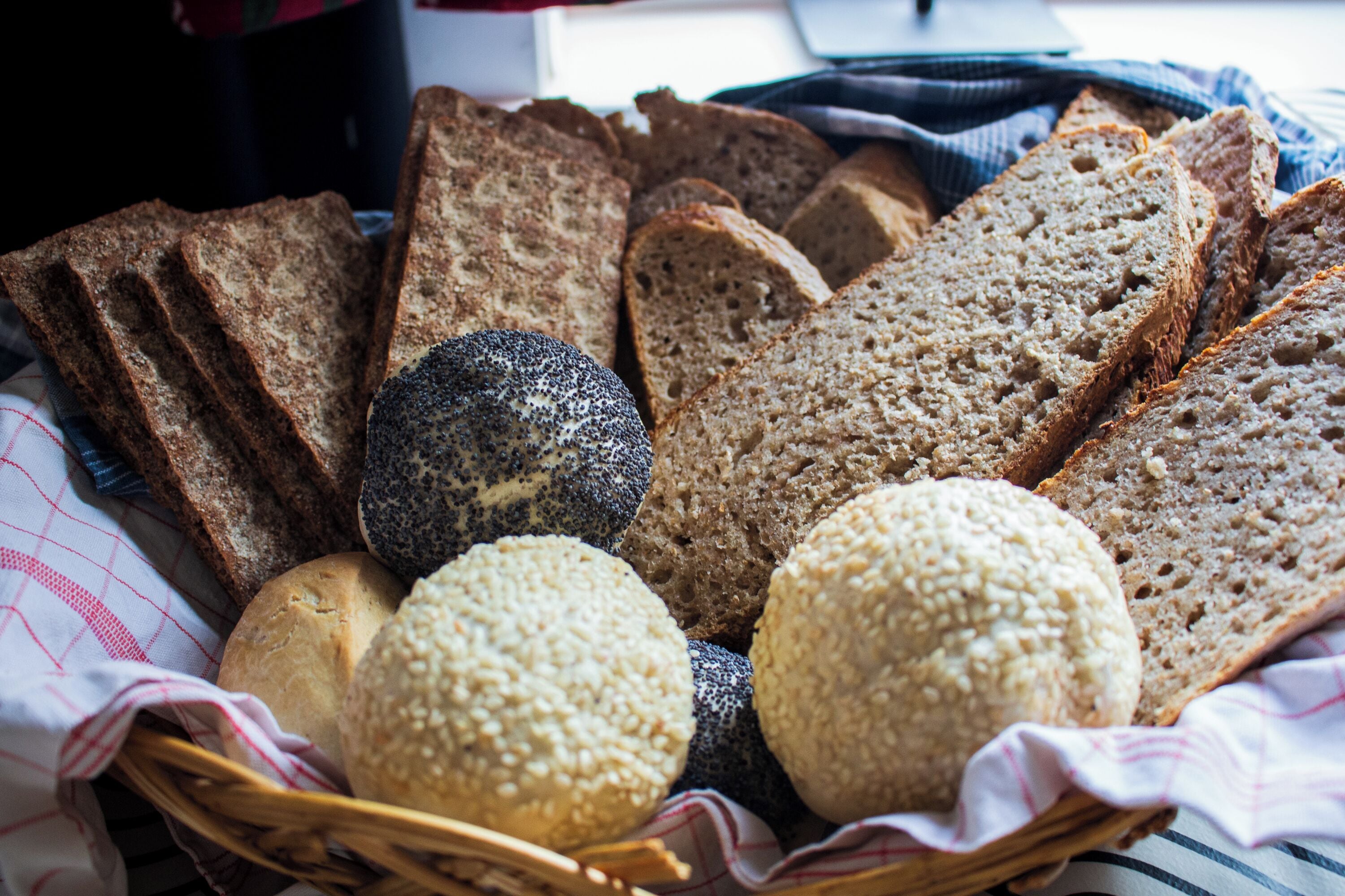 Een mand met diverse broden, waaronder volkoren, roggebrood en brood met papzaad.