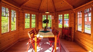 A wooden cabin with a dining area featuring a table and chairs, large windows, and a ceiling fan. - Gopshusgården - Rum och Stugor (Mora)