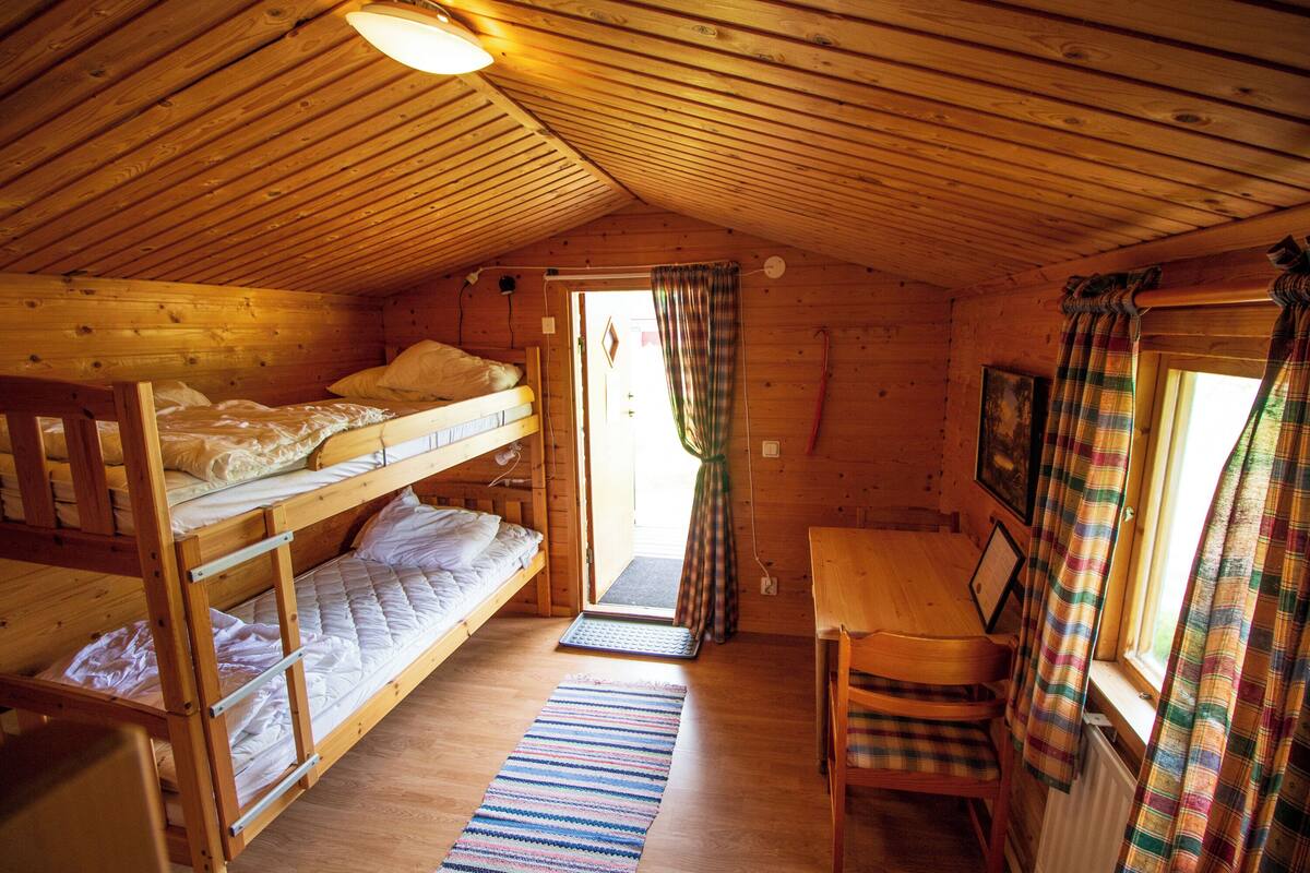 A cabin with bunk beds, a wooden table, and a window with curtains.