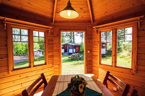 A wooden cabin with a dining table and chairs, large windows, and a view of a house and picnic table outside. - Gopshusgården - Rum och Stugor (Mora)