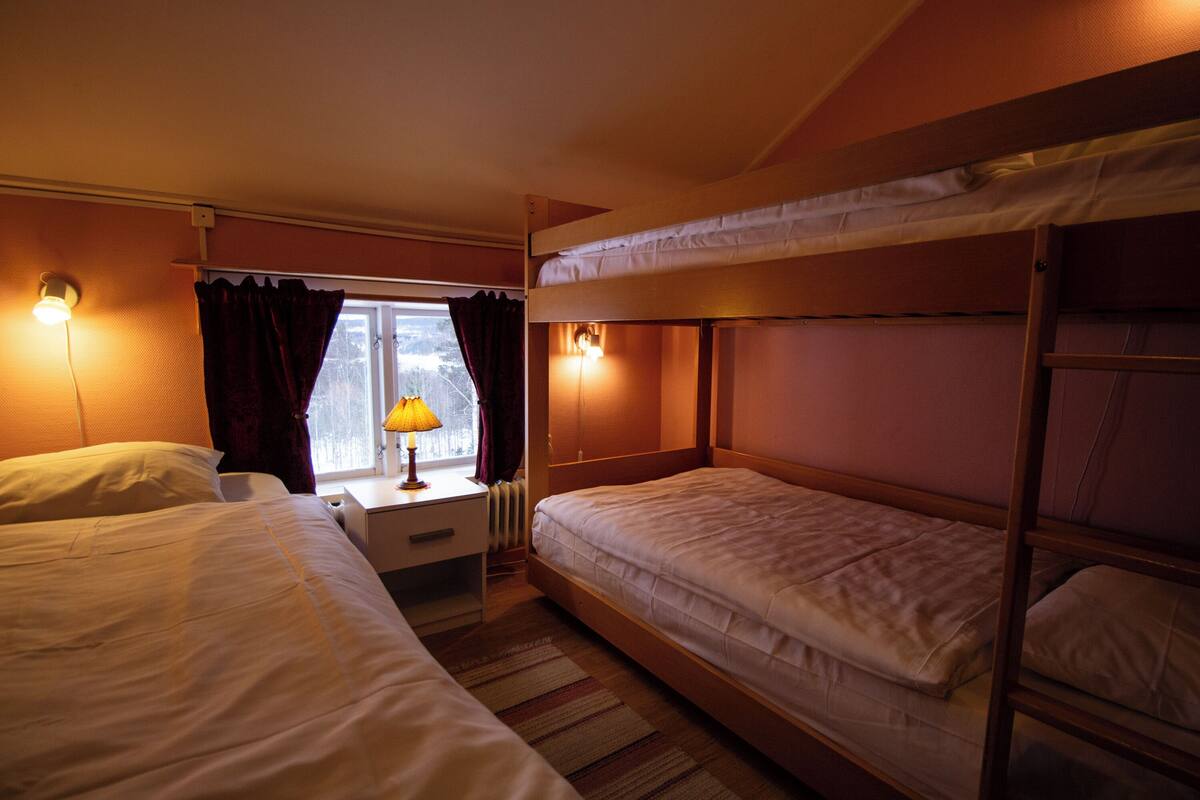 A room with bunk beds, a desk, a lamp, and a window with curtains.