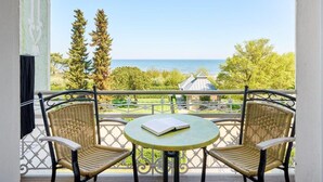 A balcony with two wicker chairs and a small round table, overlooking a scenic view of the sea and a garden. - Strandvillen Wald & See (Zinnowitz)