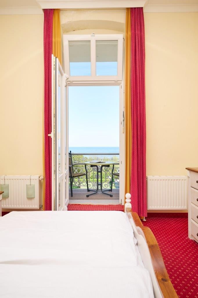 A bedroom with a bed, a window, and a view of the sea.