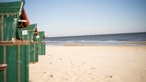 Rows of green beach chairs with numbers on them, arranged on a sandy beach with the ocean in the background. - Strandvillen Wald & See (Zinnowitz)