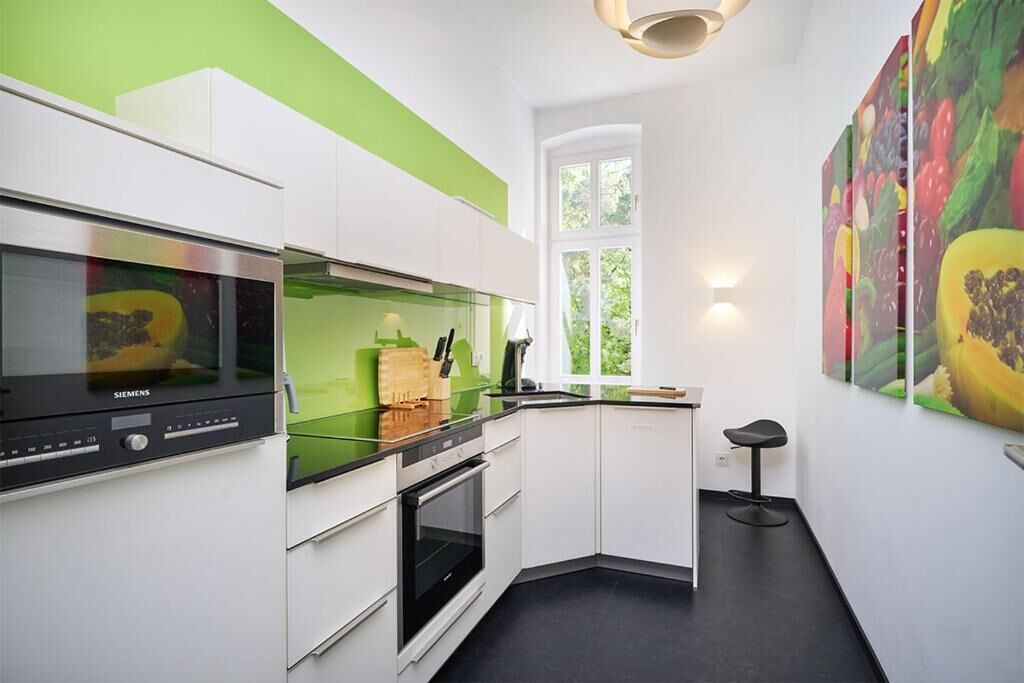A modern kitchen with white cabinets, a green countertop, a Siemens oven, and a window with a view of greenery.