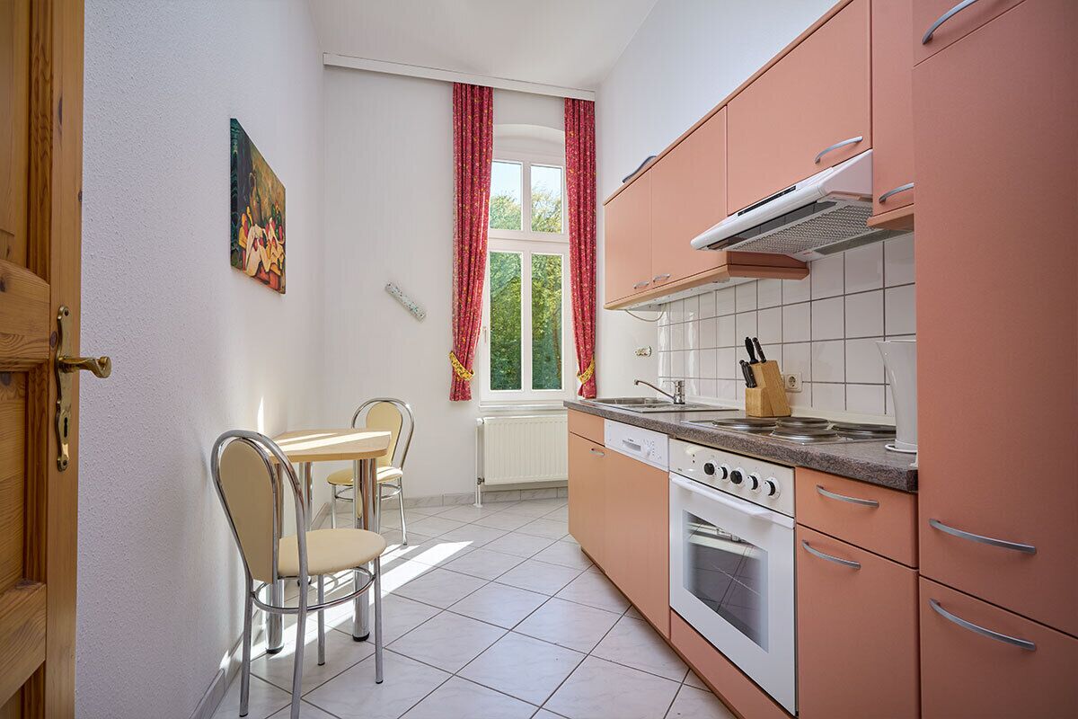 A kitchen with a stove, oven, and countertop. There is a window with curtains and a painting on the wall.