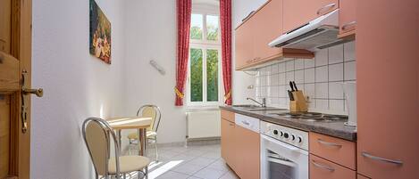 A kitchen with a stove, oven, and countertop. There is a window with curtains and a painting on the wall.