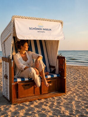 Una silla de playa con dosel, identificada con la etiqueta 'SCHÖNER INSELN', sobre una playa arenosa.