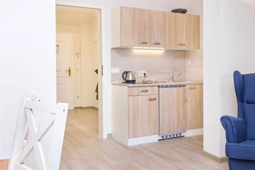 A compact kitchen with wooden cabinets, a built-in dishwasher, and a kettle on the countertop.