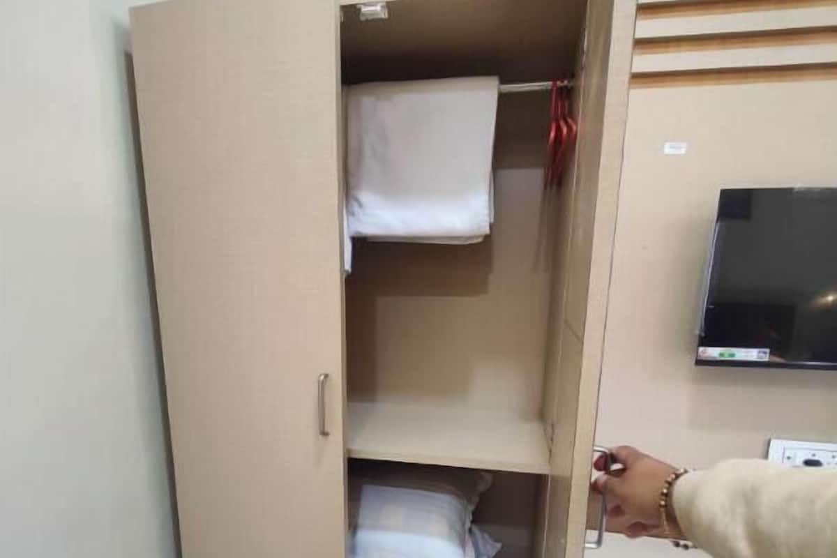 Un armario con varios estantes, un televisor en la pared y una mano alcanzando una repisa.