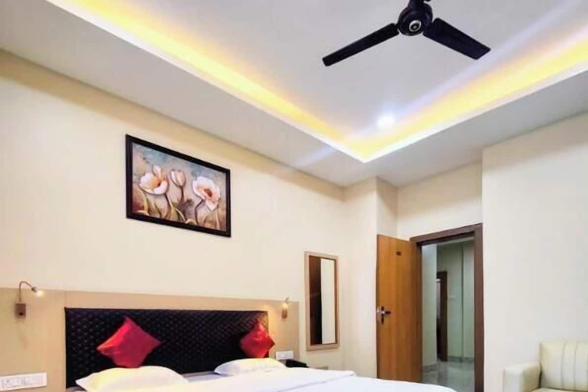 Un dormitorio con una cama, ventilador de techo, un cuadro, mesita de noche, espejo y una puerta.