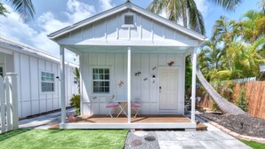 A white house with a covered porch, a small patio, and a well-maintained lawn. - Beautiful, private,  bright one bedroom cottage walk to Duval, Truman Waterfront, Santiago's Bodega (Key West)