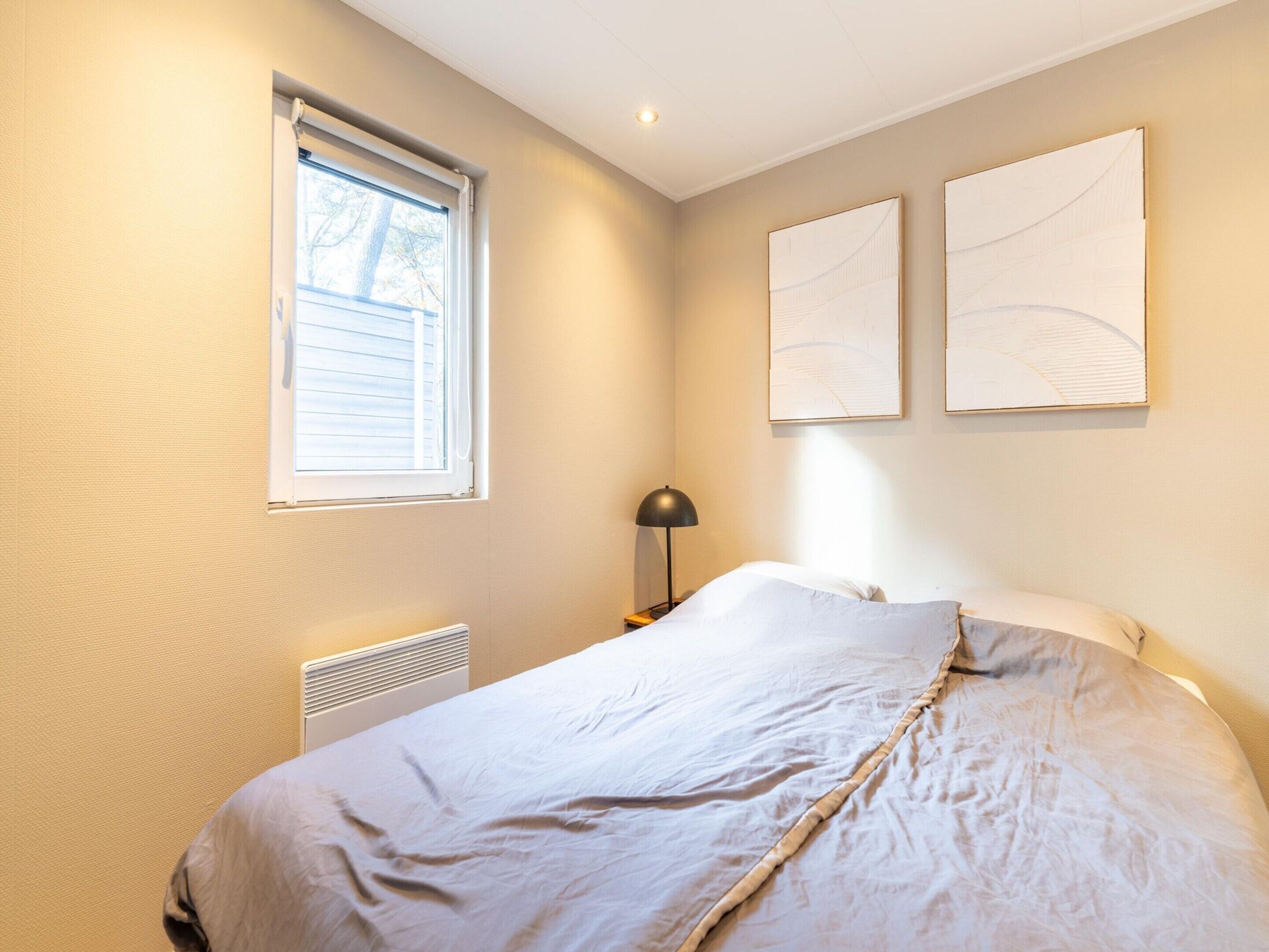 A bedroom with a bed, a window, a radiator, and two wall-mounted artworks.