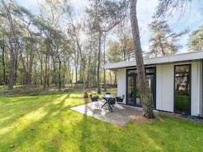 A modern house with a patio, surrounded by a forest.