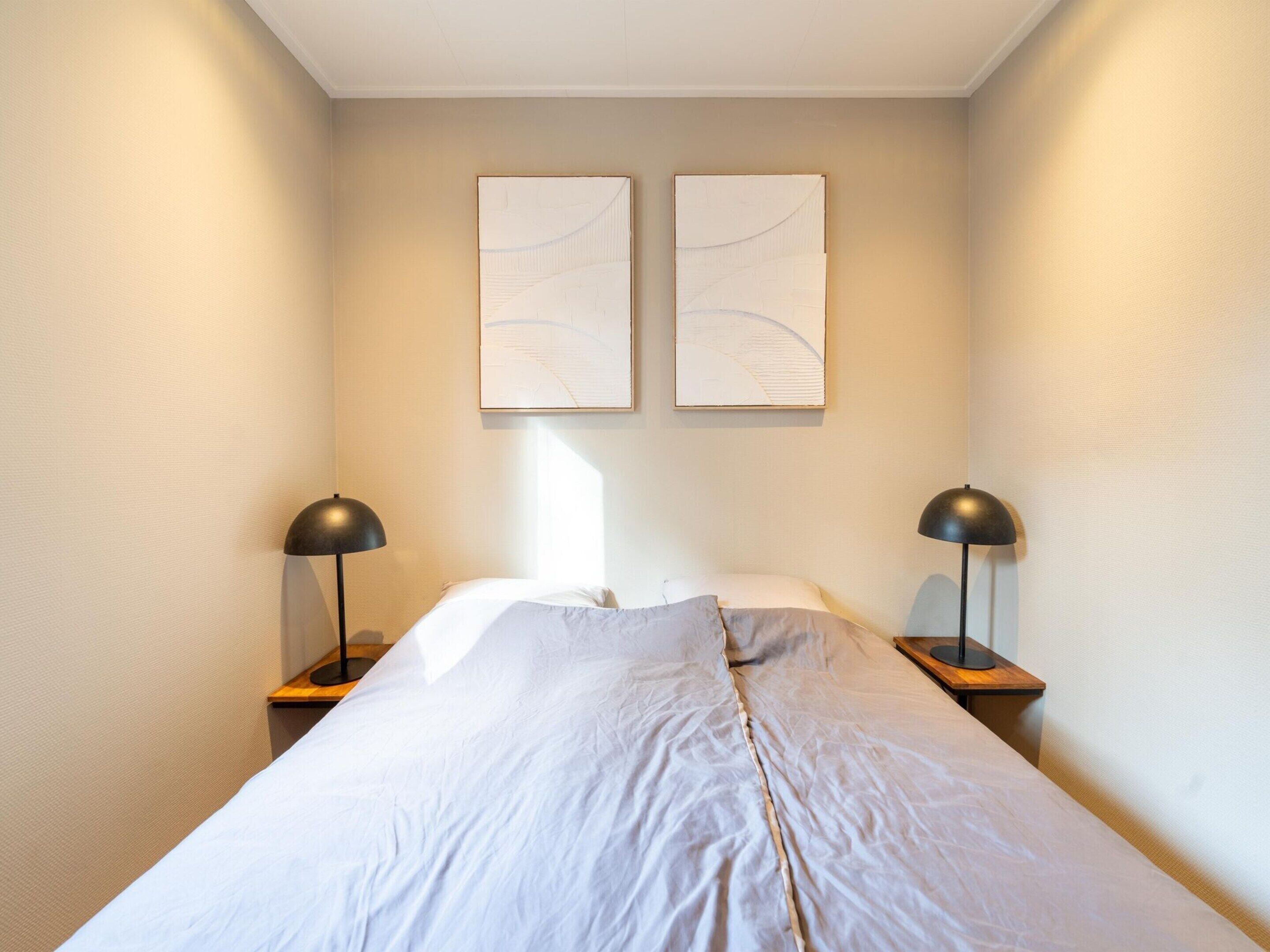 Ein ordentlich bezogenes Bett mit weißen Leinen, zwei Nachttischlampen und abstrakter Wandkunst.