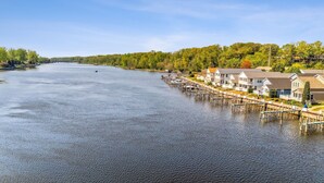 A waterfront property with docked boats, a row of houses with balconies, and a forested backdrop. - On The River, Assn Pool & Hot Tub, Water Taxi in Summer (St. Joseph)