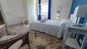 A bedroom with a bed, a small table, a chair, and a desk with a lamp. - Casa Blu Marino (Favignana)