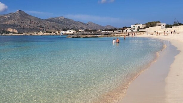 A beach with clear water, a sandy shore, and buildings in the background. - Casa Blu Marino (Favignana)