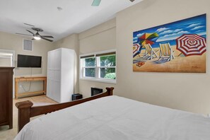 A bedroom with a bed, a wardrobe, a desk, a television, and a painting of a beach scene. - Higher Altitude 1 BR 1 BA Short walk to the beach! (Surf City)