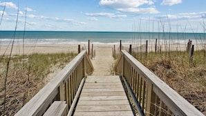 Pasarela de madera que conduce a una playa, con cielo despejado y océano al fondo.