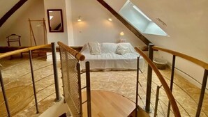 Une chambre mansardée avec un plafond en pente, un lit, un escalier en bois et une lucarne.