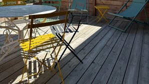 Une terrasse en bois avec une table et des chaises, un parasol vert et une vue sur des montagnes enneigées.