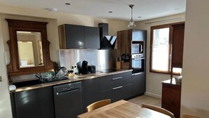 Une cuisine moderne avec des meubles de rangement aux couleurs sombres, une table à manger en bois et un four encastré.