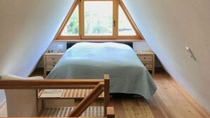 Een klein zolderkamertje met schuine kap, een enkel bed, houten vloer en een raam.