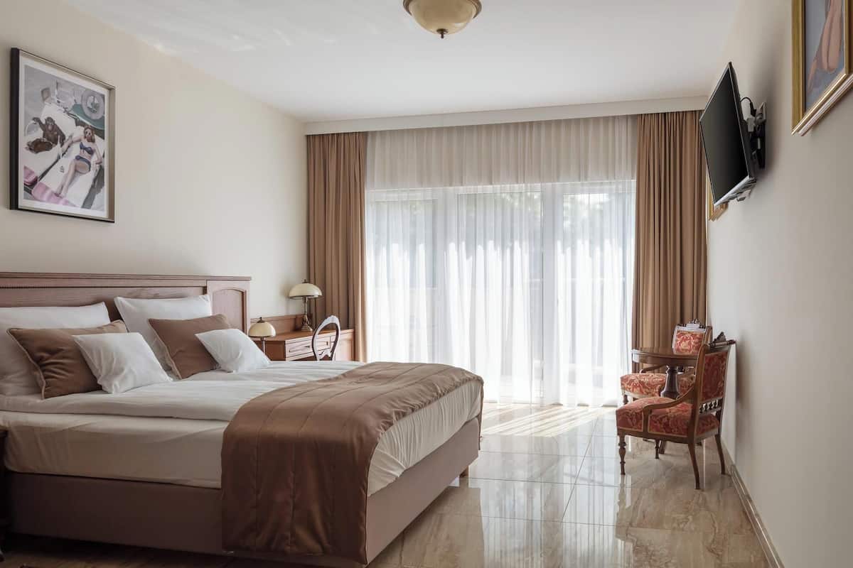 Habitación de hotel con una cama grande, un escritorio con lámpara, una silla y televisión instalada en la pared.