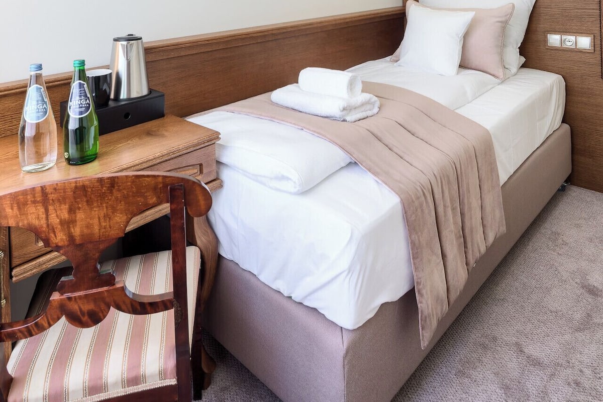 Habitación de hotel con cama, escritorio, silla, cafetera y dos botellas de agua.