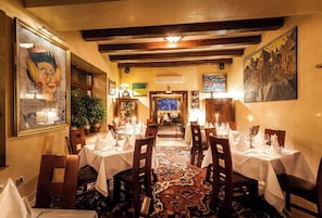 Un comedor con mesas listas para el servicio, vigas de madera en el techo y obras de arte en las paredes.