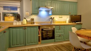 A kitchen with green cabinets, a wooden countertop, a built-in oven, and a dining area with a wooden table and white chairs. - A 2-bedroom cosy cottage based at the heart of the rural village of Brora. (Brora)